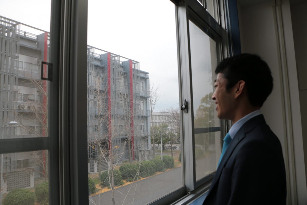 窓から外の校舎を眺める長谷川さん